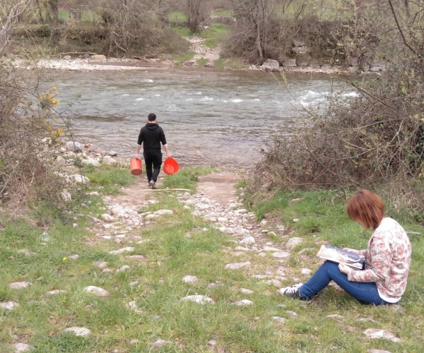 Esta imagen pretende mostrar un cambio de visión en la perspectiva de género en el acceso al agua potable: un hombre acude a un río a recoger agua mientras una mujer lee tranquilamente disfrutando de su tiempo libre.  Según datos de Médicos Sin Fronteras, cada año mueren en el mundo 800.000 personas víctimas de enfermedades provocadas por condiciones insalubres del agua. En estas situaciones son las mujeres las encargadas de recorrer largas distancias en la búsqueda de una fuente de agua limpia.   Jesús Faces Sánchez, 1 de abril de 2018, Sopeña de Cabuérniga, Cantabria.